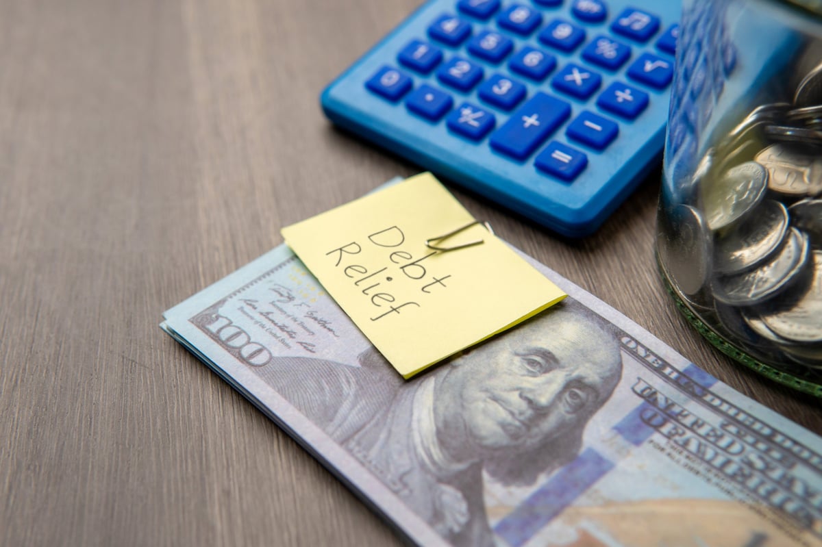 A stack of US hundred-dollar bills with a DEBT RELIEF note
